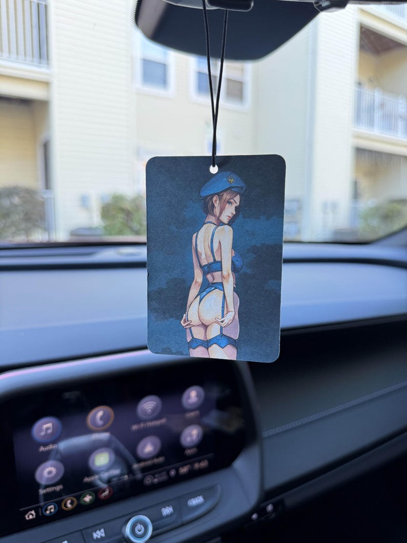 May include: Rectangular car air freshener with a blue and black illustration of a woman in lingerie and a beret. The air freshener hangs from a black string, suspended from a car's rearview mirror.