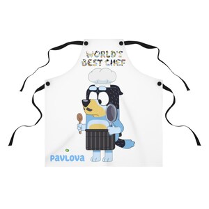 May include: A white apron with black straps features a cartoon dog wearing a chef's hat and holding a spatula. The text "WORLD'S BEST CHEF" is printed above the dog and the word "PAVLOVA" is printed below the dog.