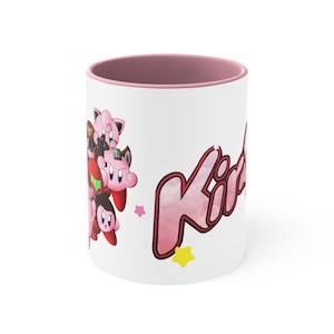 May include: A white ceramic mug with a pink rim. The mug features a pink and red cartoon character design with the word "Kirby" in a pink and red font.