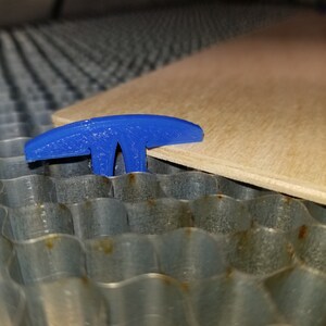 Pu&ograve; includere: Un morsetto di plastica blu a forma di T che tiene un pezzo di legno su una superficie metallica.
