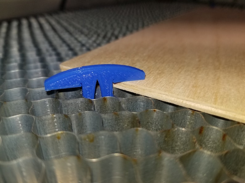 Pu&ograve; includere: Un morsetto di plastica blu a forma di T che tiene un pezzo di legno su una superficie metallica.