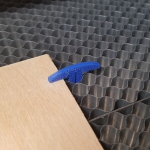 Pu&ograve; includere: Una morsetta di plastica a forma di T di colore blu viene utilizzata per tenere fermo un pezzo di legno su una superficie a nido d'ape.