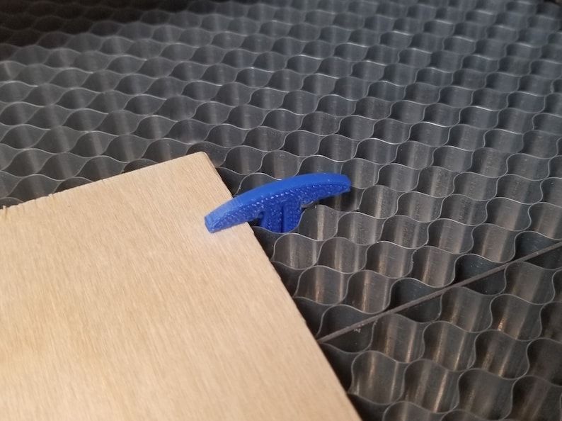 Pu&ograve; includere: Una morsetta di plastica a forma di T di colore blu viene utilizzata per tenere fermo un pezzo di legno su una superficie a nido d'ape.