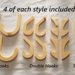 May include: A selection of wooden hooks in three designs: Hose Hooks, Double Hooks, and Single Hooks. Each style includes four pieces. The hooks are made of light-coloured wood and are arranged on a white surface. The text "4 of each style included" is visible.