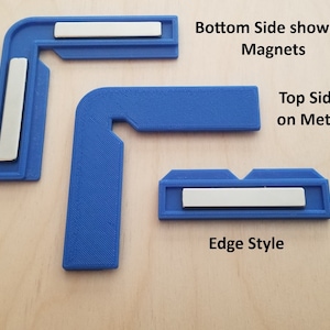 Op de afbeelding: Blauwe kunststof hoekbeugels met magneten aan de onderkant. De bovenkant is ontworpen om op een metalen laserbed te worden geplaatst. De afbeelding toont de rand stijl van de beugels.