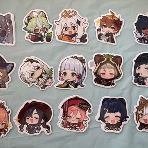 May include: A collection of colorful anime-style stickers featuring various characters. Each sticker showcases a unique character design with detailed facial expressions and outfits. The stickers are on a light blue surface.