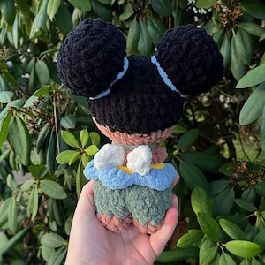 K&ouml;nnte beinhalten: Eine geh&auml;kelte Puppe mit schwarzen Haaren in zwei Knoten, die ein gr&uuml;nes Kleid mit blauen und gelben Akzenten und wei&szlig;en Fl&uuml;geln tr&auml;gt.