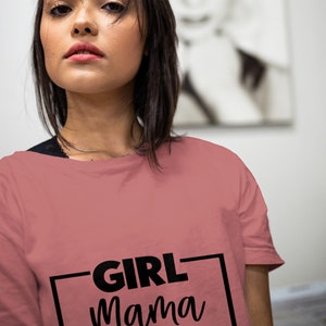 Peut inclure: Un t-shirt rose poussiéreux avec un cadre noir autour du texte "GIRL mama" imprimé sur le devant.