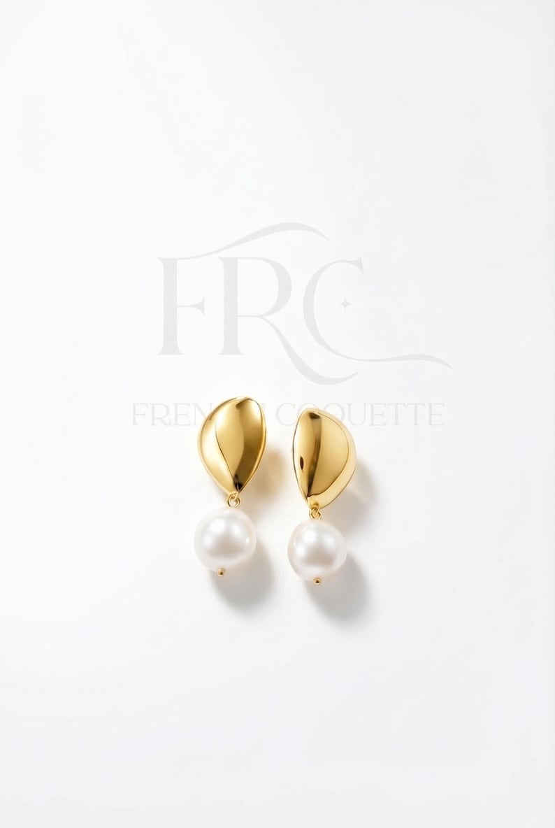May include: A pair of gold-colored earrings with a teardrop-shaped top and a large, round, white pearl hanging below. The earrings are displayed on a white background.