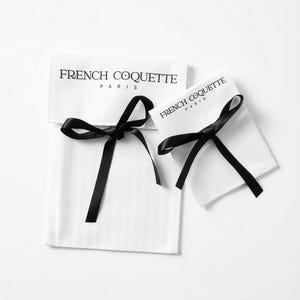 Puede incluir: Dos bolsas de tela blanca con cierres de cinta de raso negro. El texto "FRENCH COQUETTE PARIS" est&aacute; impreso en negro en la parte delantera de cada bolsa. Probablemente para joyas o peque&ntilde;os regalos.