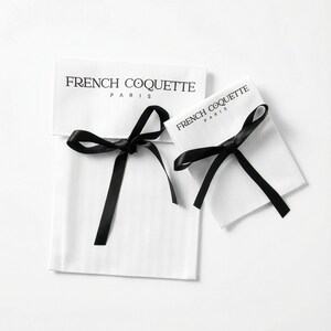 May include: Two white fabric pouches with black satin ribbon closures. The text "FRENCH COQUETTE PARIS" is printed in black on the front of each pouch. The pouches are likely for jewelry or small gifts.