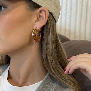 Peut inclure: Boucles d'oreilles créoles dorées avec un motif écaille de tortue. Ces boucles d'oreilles de taille moyenne ont une finition polie. Les créoles sont un accessoire classique, adapté au quotidien ou aux occasions spéciales.