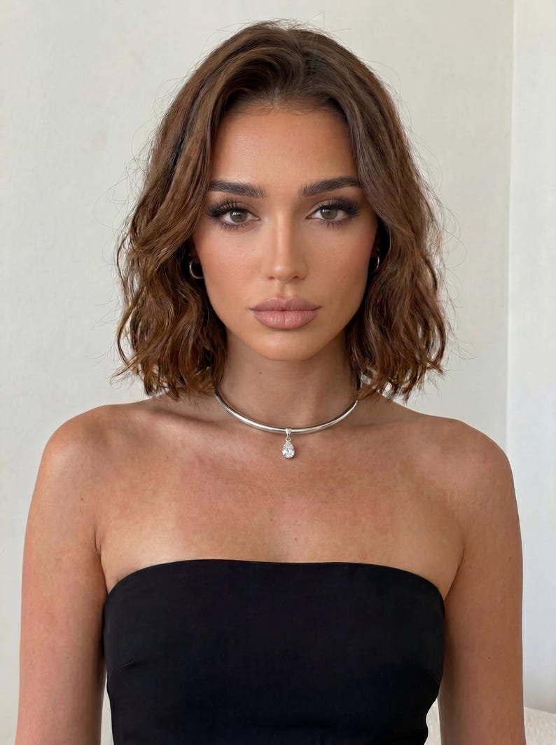 Puede incluir: Un collar de gargantilla plateado con un colgante en forma de l&aacute;grima. La modelo lleva un top negro sin tirantes. La mujer tiene el pelo casta&ntilde;o y mira a la c&aacute;mara. El fondo es una pared blanca lisa.
