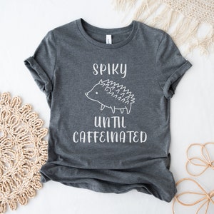 May include: A dark gray t-shirt with a white graphic of a hedgehog and the text "Spiky until caffeinated".