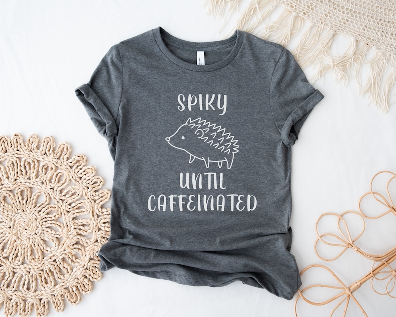 May include: A dark gray t-shirt with a white graphic of a hedgehog and the text "Spiky until caffeinated".