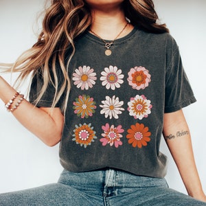 May include: A dark gray t-shirt with a vintage-style floral print. The flowers are in shades of pink, orange, yellow, and green. The shirt has a crew neck and short sleeves.