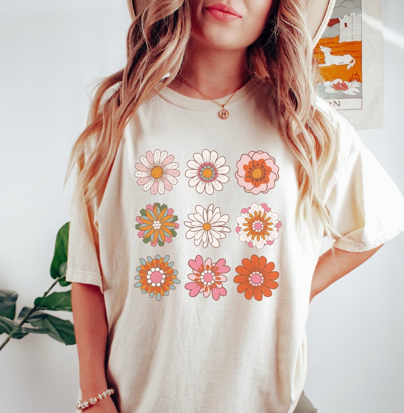 May include: A white t-shirt with a retro design featuring nine colorful flowers in a grid pattern.