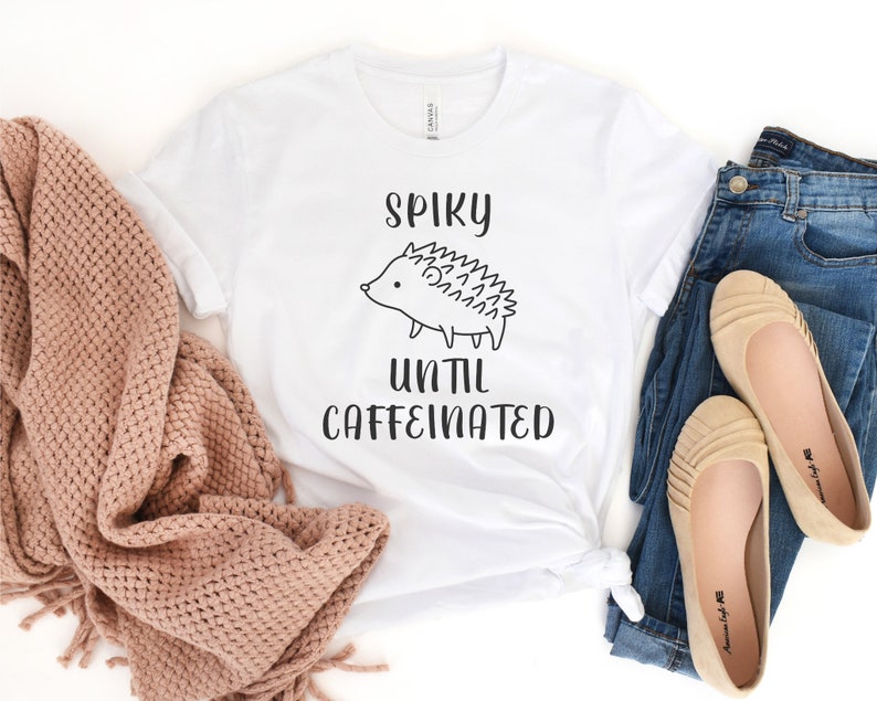 May include: White t-shirt with a black and white illustration of a hedgehog and the text "Spiky until caffeinated".