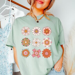 May include: A light green t-shirt with a retro floral design. The design features nine different flowers in shades of pink, orange, yellow, and green.