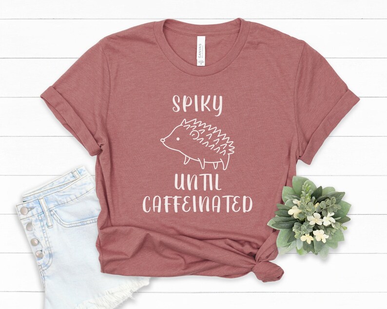 May include: A maroon t-shirt with a white graphic of a hedgehog and the text "Spiky until caffeinated".
