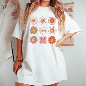 May include: A white oversized t-shirt with a retro design featuring nine colorful flowers in a grid pattern.