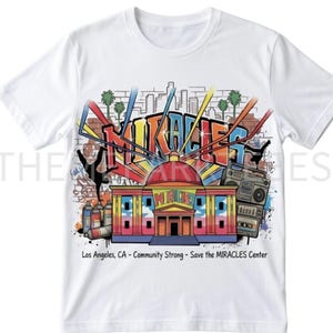 May include: White t-shirt featuring a colorful graphic design. The design includes the word "MIRACLES" in bold letters, a building with a red dome, graffiti art, and a boombox. Text at the bottom reads "Los Angeles, CA - Community Strong - Save the MIRACLES Center."