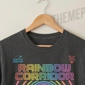 Puede incluir: Una camiseta gris carb&oacute;n de manga corta con el texto RAINBOW CORRIDOR en una fuente estilo ne&oacute;n sobre semic&iacute;rculos conc&eacute;ntricos de colores del arco&iacute;ris. Un peque&ntilde;o icono de estrella fugaz y una cabeza de animal estilizada aparecen arriba.