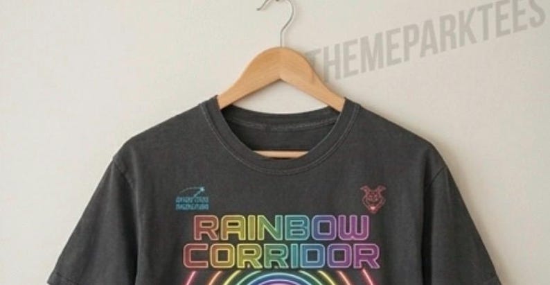 Puede incluir: Una camiseta gris carb&oacute;n de manga corta con el texto RAINBOW CORRIDOR en una fuente estilo ne&oacute;n sobre semic&iacute;rculos conc&eacute;ntricos de colores del arco&iacute;ris. Un peque&ntilde;o icono de estrella fugaz y una cabeza de animal estilizada aparecen arriba.