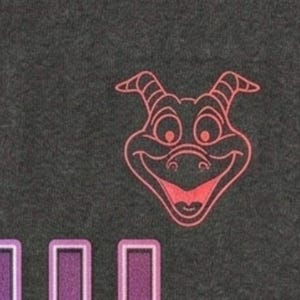 Puede incluir: Una tela gris oscuro que presenta una ilustraci&oacute;n de l&iacute;neas color coral de una cabeza de drag&oacute;n con cuernos y una amplia sonrisa, situada sobre un gr&aacute;fico parcial con letras en degradado morado y azul que tienen un borde blanco.