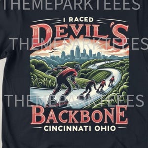 May include: Black t-shirt featuring a graphic of inline skaters racing on a winding road. The design includes the text "I Raced Devil's Backbone Cincinnati Ohio" in red and white, with a cityscape and sunset in the background.