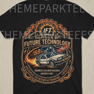 May include: Black t-shirt featuring a graphic design with the text "TINO YRVELER OF FUTURE TECHNOLOGY". The design includes a car, flames, and gears. The shirt also has the text "ADVANCED FLUX-DRIVE RESEARCH".