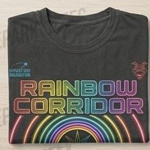 Puede incluir: Una camiseta negra de cuello redondo con el texto RAINBOW CORRIDOR en una fuente de degradado multicolor. Debajo del texto hay un gr&aacute;fico de un arco&iacute;ris multicolor. Un peque&ntilde;o icono de estrella fugaz est&aacute; a la izquierda y un icono de cabeza a la derecha.