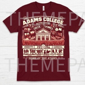 May include: Maroon t-shirt with a vintage design for Adams College Homecoming Greek Games '84. The graphic includes a building, flags, and figures, with text reading "Home of the Atoms".