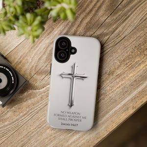 May include: A white phone case with a silver cross and the text "No weapon formed against me shall prosper Isaiah 54:17".