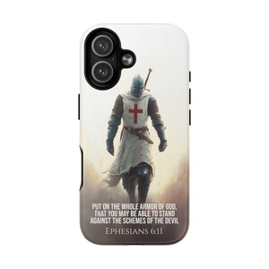 May include: A phone case featuring a digital illustration of a knight in armor with a red cross on his chest. The background is a soft, blurred landscape. Text at the bottom reads "PUT ON THE WHOLE ARMOR OF GOD, THAT YOU MAY BE ABLE TO STAND AGAINST THE SCHEMES OF THE DEVIL EPHESIANS 6:11."