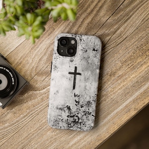 May include: A white phone case with a black cross design and a distressed, textured finish. The case has a black camera bump with three lenses.