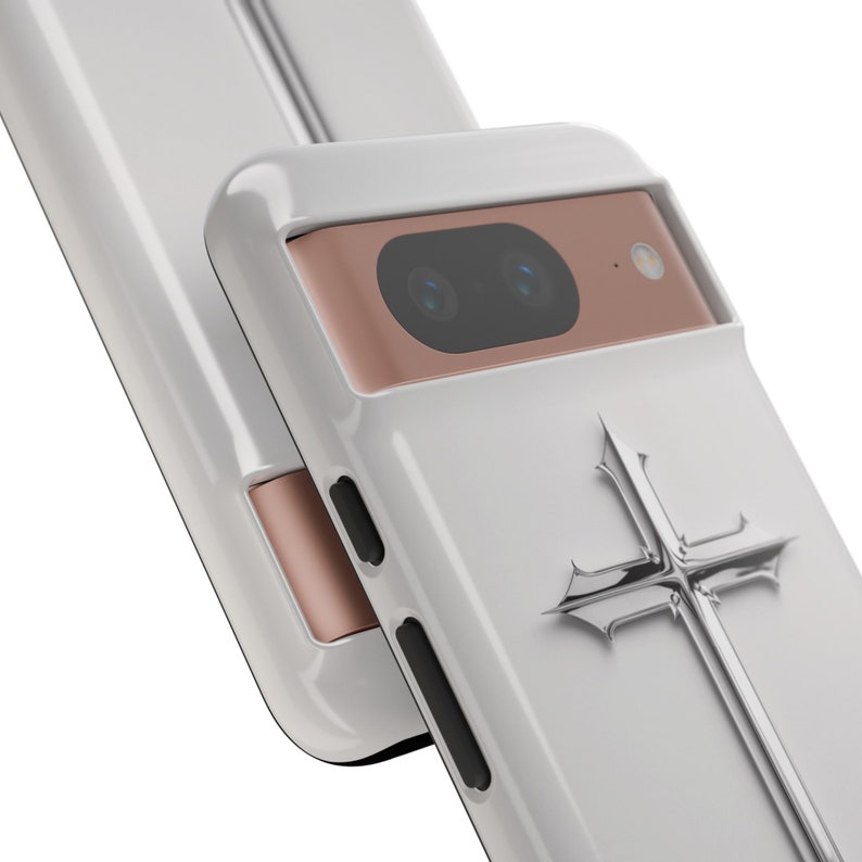 May include: White phone case with a silver cross design and a rose gold camera housing.