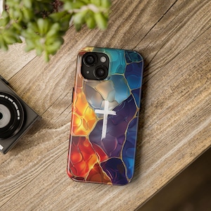 May include: A colorful phone case with a white cross design. The case has a stained glass look with shades of red, orange, yellow, blue, and purple.