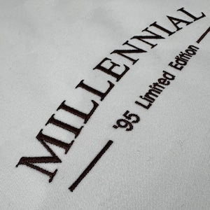 May include: White fabric with brown embroidered text that reads "MILLENNIAL - '95 Limited Edition - "