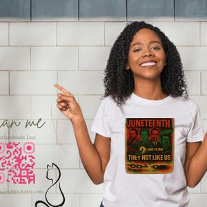 May include: White t-shirt featuring a graphic with the text "Juneteenth" and "They Not Like Us". The graphic includes images of four men. A QR code and the text "Scan me" are also visible.