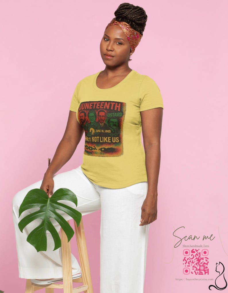 May include: A woman wearing a yellow t-shirt with a graphic that reads "Juneteenth" and "Hey Not Like Us." The shirt features a vintage-style design with portraits and text. She is wearing white pants and a patterned headscarf.