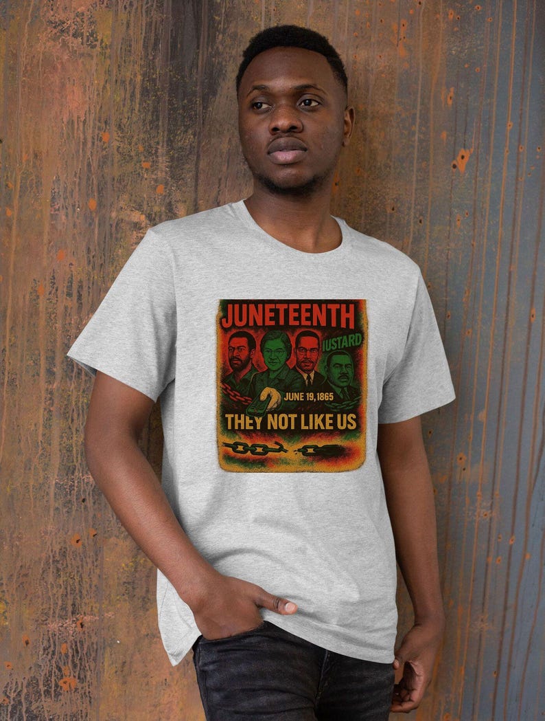 May include: A gray t-shirt featuring a graphic with the text "Juneteenth" and "They Not Like Us." The graphic includes images of four men and the date June 19, 1865. The shirt is worn by a person.