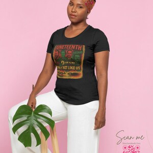 May include: Black t-shirt with a graphic featuring the text "Juneteenth" and the phrase "They Not Like Us." The design includes portraits and the date June 19, 1865. The woman is wearing a patterned headscarf and white pants.