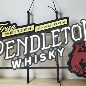 May include: A neon sign for Pendleton Whisky. The sign features the words "True Western Tradition" and "Pendleton Whisky" in a stylized font. A red bucking bronco graphic is on the right side. The sign is black with white and yellow accents.