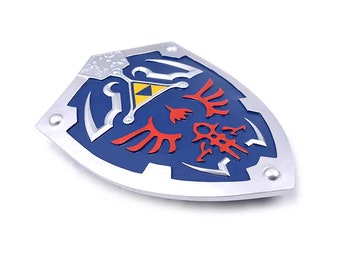 May include: A shield-shaped metal pin featuring a blue enamel background with a silver border. The design includes a yellow triangle at the top, red wing-like symbols in the center, and silver accents throughout the surface of the shield.