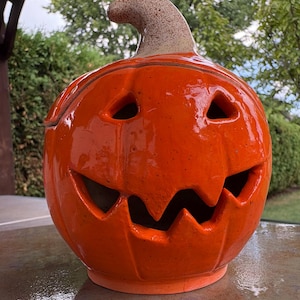 Peut inclure: Une lanterne en forme de citrouille en céramique orange brillante. Elle présente des yeux triangulaires et une bouche en zigzag. La tige est de couleur marron clair. Décoration d'Halloween.
