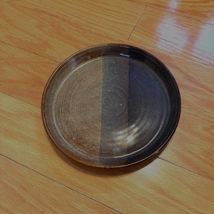 May include: A brown and blue ceramic plate with a swirl design. The plate is round and has a slightly raised rim.