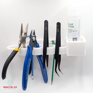 May include: A white 3D-printed tool organiser rack featuring multiple slots holding various tools including needle-nose pliers, blue side cutters, two black ESD-10 and ESD-15 tweezers, and a white glue stick labelled with application materials.