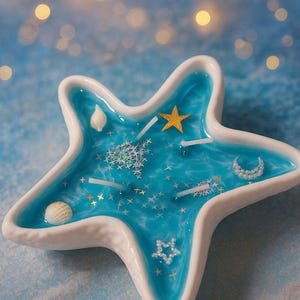 May include: A starfish-shaped candle holder with a white rim and a blue interior. The candle holder is decorated with seashells, stars, and a crescent moon. The candle holder has three white candles and a gold star.