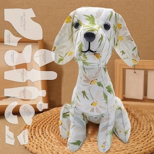 May include: A stuffed dog with a white floral pattern featuring yellow and green accents. The dog is sitting upright with black eyes and a black nose. Sewing patterns are visible in the background.